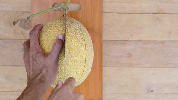 The man use knife split the yellow galia melon on wood plate