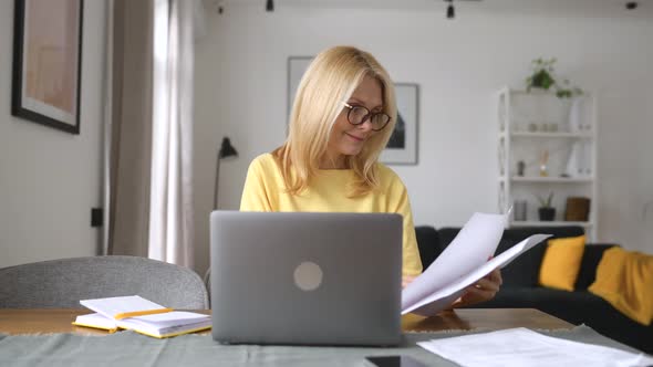 Concentrated Middleaged Woman Sitting at the Desk and Looking at the Documents