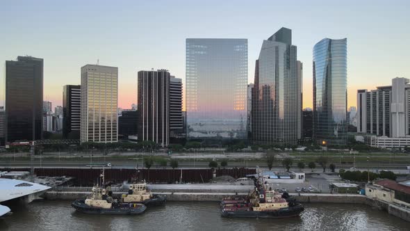 Aerial dolly out of boats in Puerto Madero docks with high-rise buildings in background at sunset, B