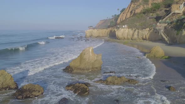 Aerial shots of El Matador beach over breaking waves and rocks on a hazy summer morning in Malibu, C