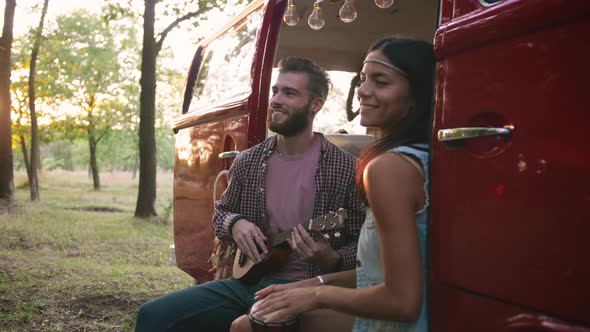 Happy Young Mixed Race Couple Playing Instruments and Having Some Fun in Retro Hippie Minibus in