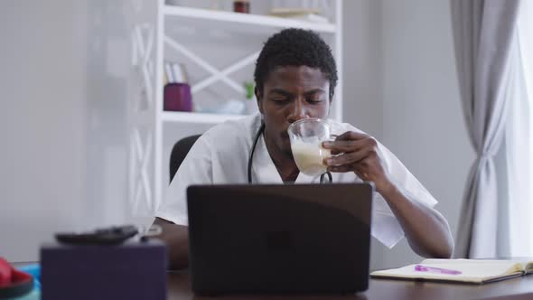 Front View Focused Smart African American Doctor Drinking Morning Coffee Surfing Internet on Laptop
