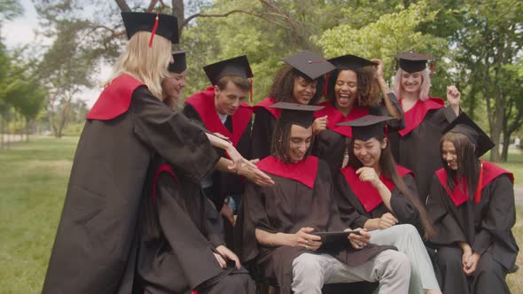 Joyful Multiracial Graduates in Academic Gowns Working on Tablet Pc After Graduation Ceremony