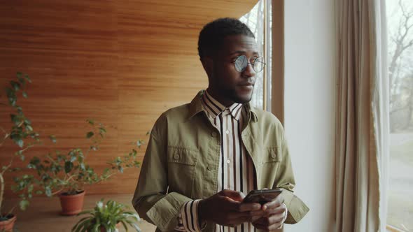 Afro-American Man Typing on Phone in Library Auditorium