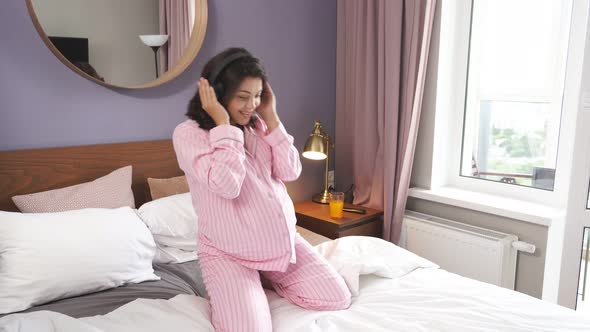 Positive Pregnant Woman Enjoy Music in Headphones Relaxing on Bed at Home