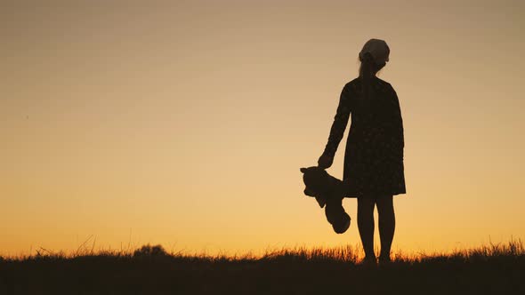 Little Girl in Dress Holding Teddy Bear Toy at Sunset. Silhouette of a Child with a Toy. Concept of