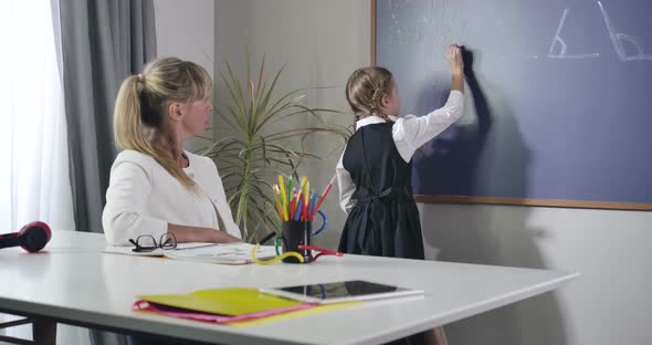 Portrait of Adult Caucasian Teacher Dictating Formula To Little Girl Writing on Blackboard