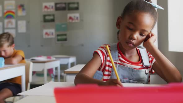 Video of thoughtful african american girl sitting at desk in classroom