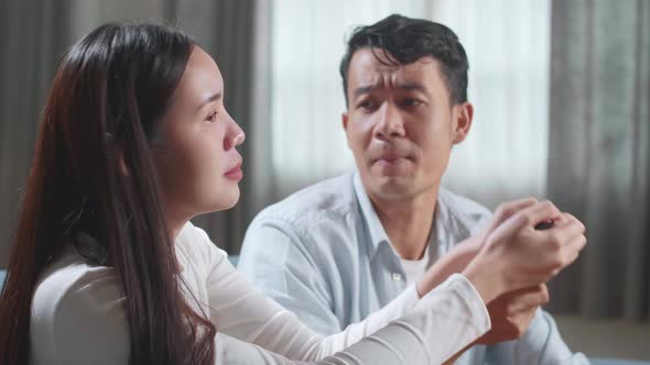 Young Asian Couple Is Watching Tv At Home. Man Switches Channels, Woman Selects Control