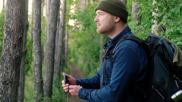 Man with a large backpack travels uses a compass to navigate in the forest