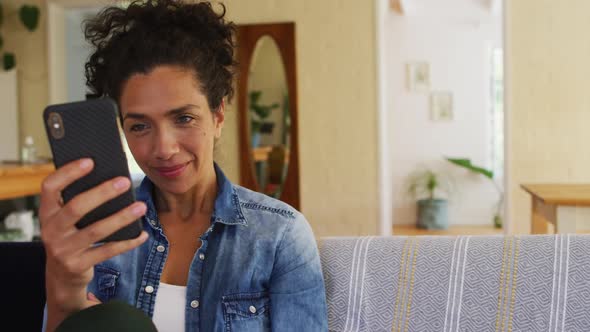 Caucasian woman using smartphone on video call, sitting on sofa at home