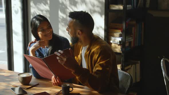 Front view of young mixed-race couple discussing over menu card in cafe 4k