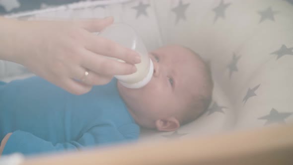 Newborn Kid Eats Milk Mix From Bottle Held By Mom in Cocoon