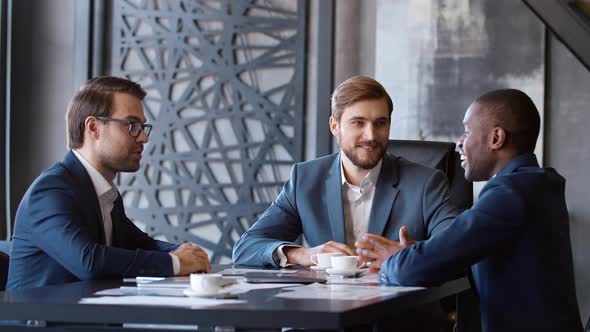 Three business partners in suits smiling and chatting at a meeting