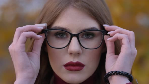 Portrait of a Beautiful Young Woman Putting on Glasses While Looking at the Camera