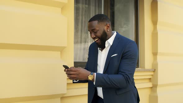 Smiling Afro Businessman Texting Message Outdoors