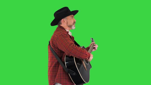Man in a Cowboy Hat Singing and Playing the Guitar While Walking on a Green Screen Chroma Key