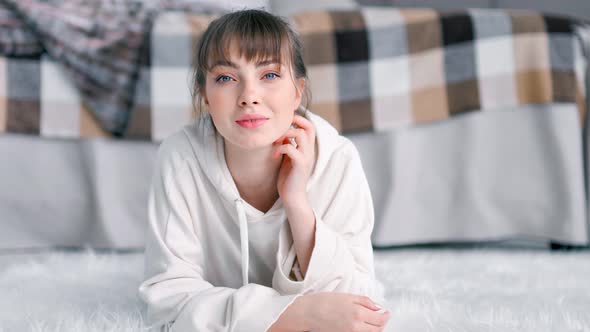 Portrait of Smiling Domestic Woman Lying on White Fluffy Carpet in Bedroom