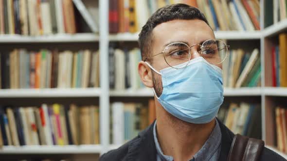 Man in Mask Looking at Bookshelves in Library alt