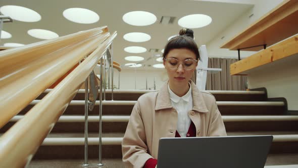 Woman Using Laptop on Library Stairs