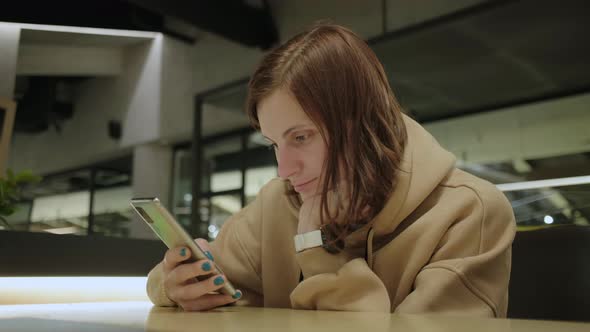 Young Woman Using Mobile Phone for Searching Internet Sitting in Cafe