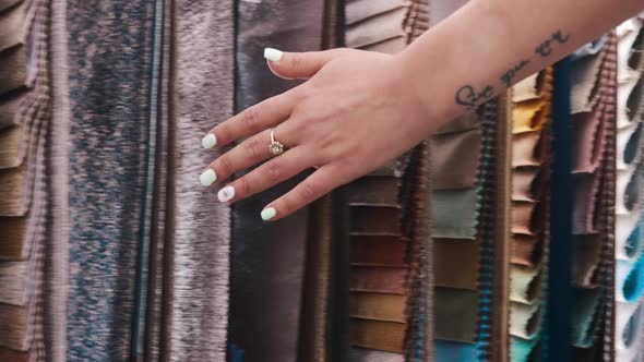 A Woman with Nails Done Runs Her Hand Along the Hung Fabrics with Ornaments