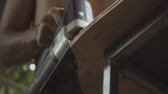 craftsman using an electric jigsaw to shape a skateboard deck from plywood by hand. No recognizable