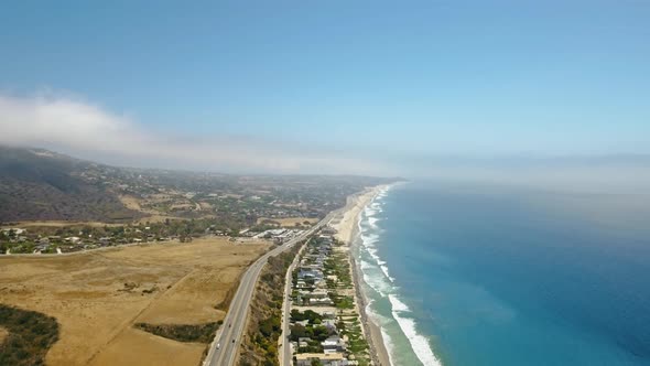 Ocean and coast with a road and cars, a settlement and fields in Malibu, California, USA