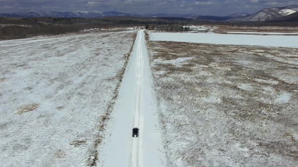 View From a Drone on a Winter Road in a Field Along Which a Car Is Driving