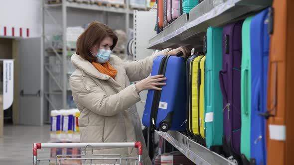 Woman in Mask Looking at Suitcase in Supermarket