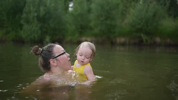 Little Funny Cute Blonde Girl Child Toddler in Yellow Bodysuit Laughing Learns Swim Outside at