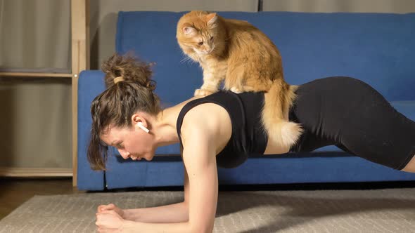 Strong Woman Does Plank Exercise While Red Cat Sits on Back