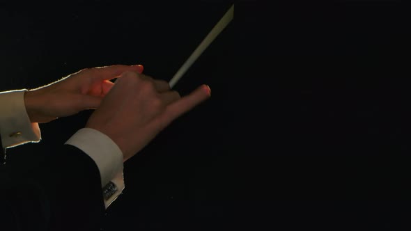 Moving Hands of an Orchestra Conductor Directing Musicians with Movement of Baton on Black