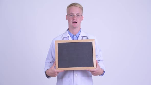 Happy Young Blonde Man Doctor Talking While Holding Blackboard