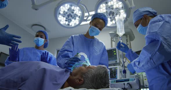 Mixed race surgeons wearing protective clothing putting patient to sleep in operating theatre