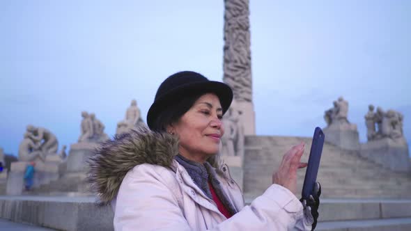 Asian woman standing and taking a photo in public Frogner park, Norway