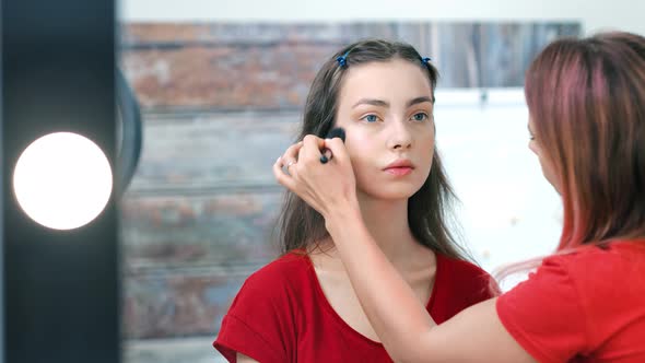 Professional Female Makeup Artist Working with Young Pretty European Woman Using Brush