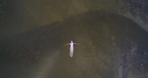 Woman in white dress lies on water of lake reflecting sky