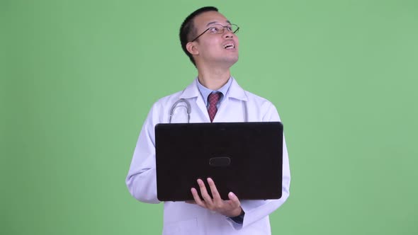 Happy Asian Man Doctor Thinking and Talking While Using Laptop