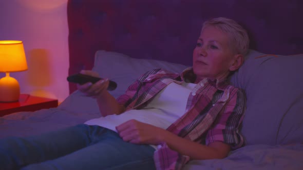 Senior Woman Lying on Bed and Changing Channels on Tv