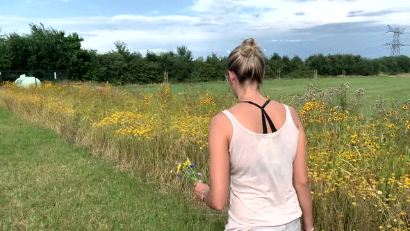 Girl walks over the meadow and collects flowers for the bouquet in the nature. 4K shot. Netherlands.