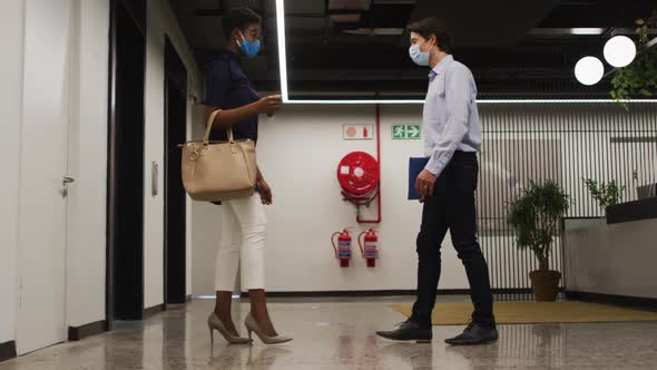 Diverse business people wearing face masks greeting in corridor using feet