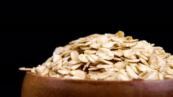 Rolled oats in wooden bowl. Dry whole grain oatmeal on black background. Macro