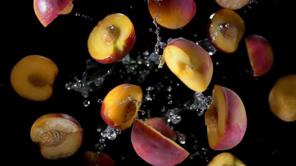 Halves of a Wet Peach are Bouncing in Splashes of Water on a Black Background