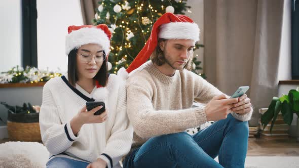 Young Mixed Race Pair Laughing Using Smartphones Sitting on Floor in Living Room Against Decorated