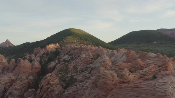 Slow tracking drone flies over sunset rocky bluffs with green grassy hills in Zion National Park