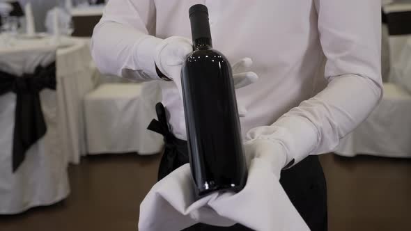 Closeup of a Waiter Wearing White Gloves Holding a Bottle of Red Wine