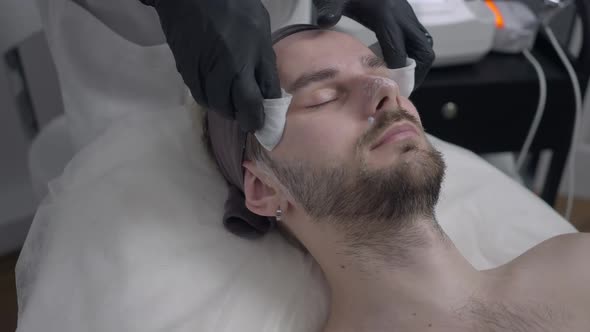 Beautician Taking Off Facial Cream Leftovers From Face Skin of Male Client in Beauty Parlor