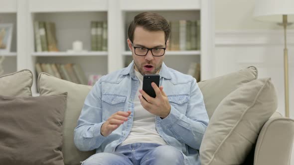 Excited Young Man Celebrating on Smartphone at Home