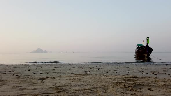 A Thailand long boat in the ocean on a misty morning with the waves crashing